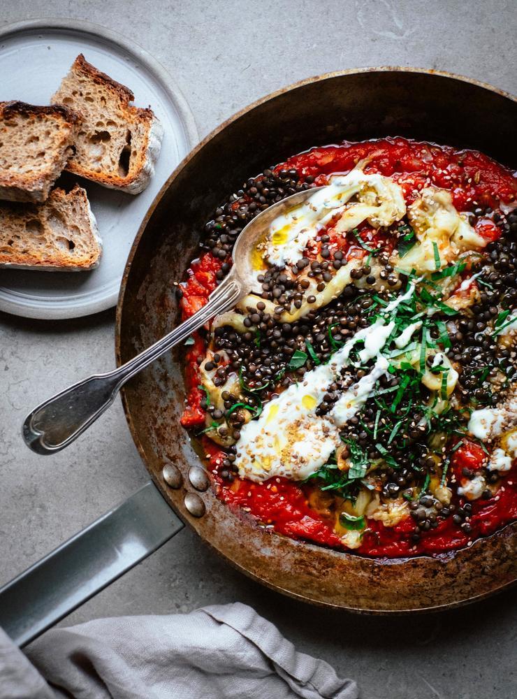 Shakshuka med aubergine och linser serverat med bröd.